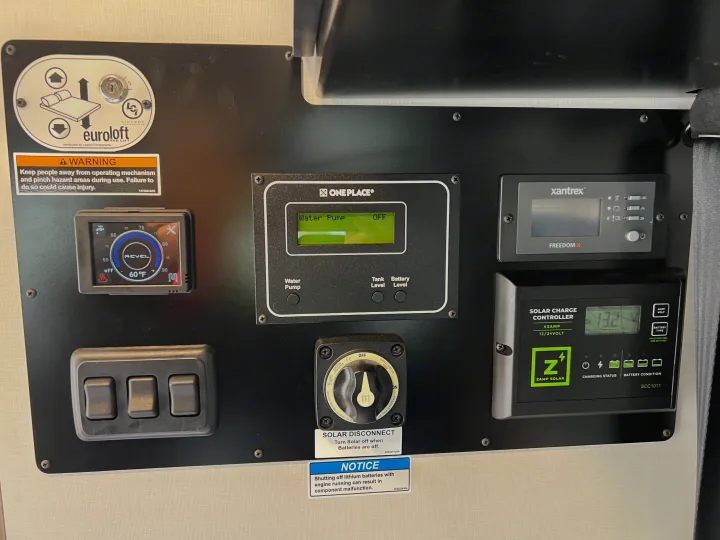 RV rental control panel: displays for water, solar, battery; switches for pump & Euroloft bed lift. Comprehensive RV management.. Winnebago Revel 2023