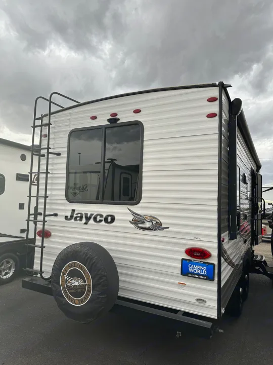 Rear view of a white Jayco travel trailer, featuring a ladder, spare tire, and large window. A great option for an RV rental.. Jayco Flight 2020