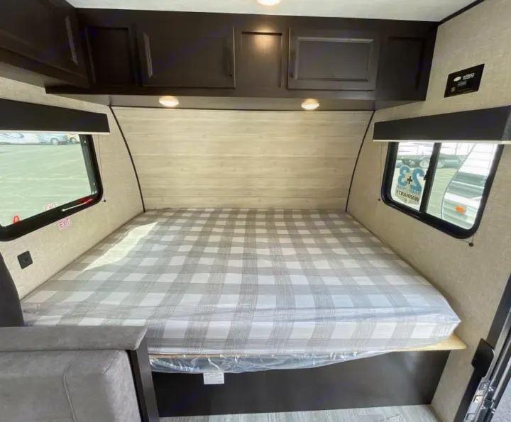 Cozy RV rental bedroom with a plaid mattress, overhead cabinets, and windows. Ideal for comfortable travel.. Jayco Jay Flight 2023