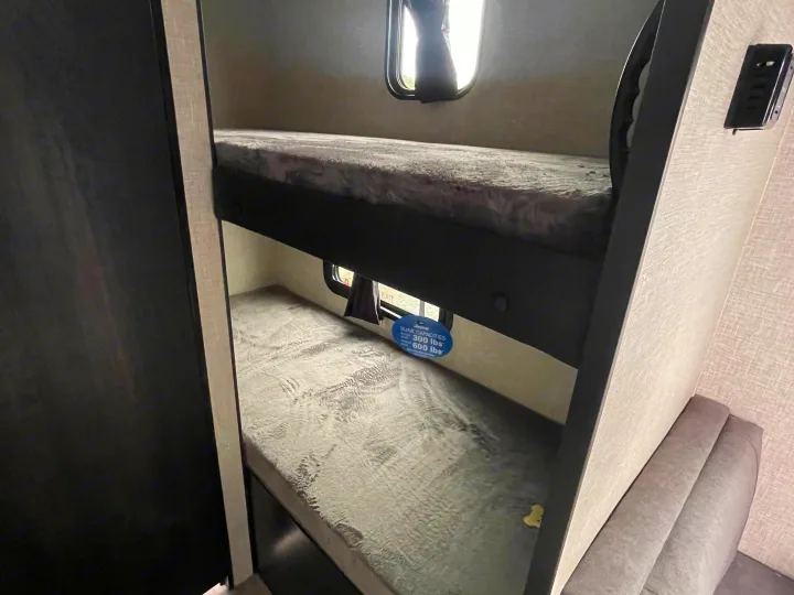 Cozy bunk beds in an RV rental, featuring individual windows and clear weight capacity labels, ideal for compact sleeping.. Jayco Jay Flight 2023