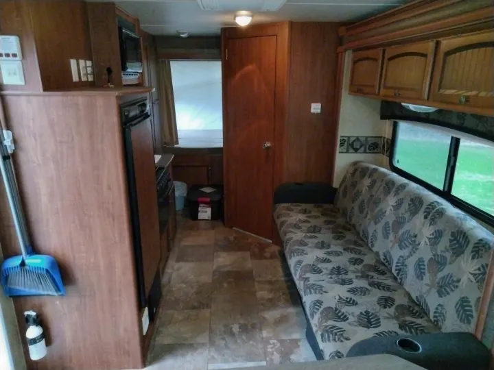 RV rental interior: A cozy living area with a leaf-patterned sofa, compact kitchen, and door to the sleeping quarters.. Jayco Jay Feather Ultra Lite 2013