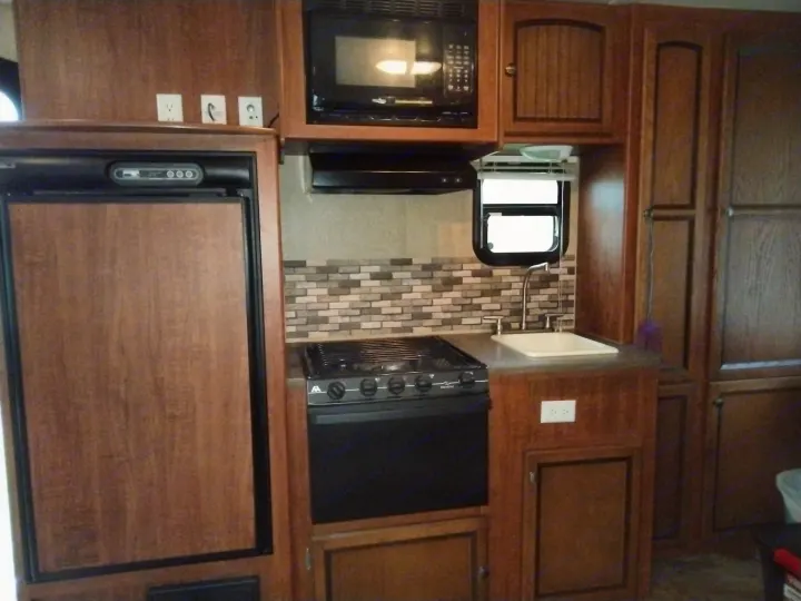 Explore this RV rental's kitchen: a cozy space with a fridge, microwave, stove, sink, and ample wood-toned cabinets.. Jayco Jay Feather Ultra Lite 2013
