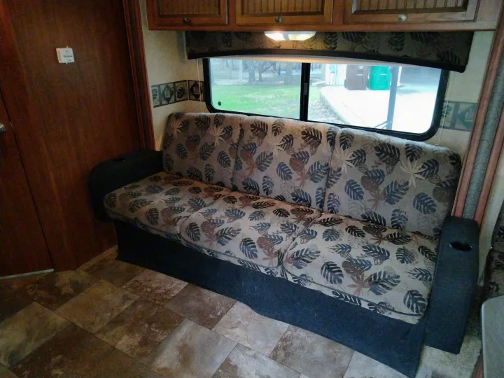 RV rental interior showcasing a spacious sofa with a tropical leaf pattern, large window, wooden cabinets, and tile flooring.. Jayco Jay Feather Ultra Lite 2013