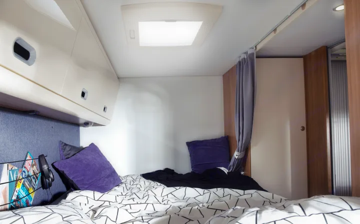 Cozy RV rental bedroom with geometric bedding, purple pillows, overhead storage, and a bright skylight for comfortable travel.. SunLiving A 75 DP 23 2023