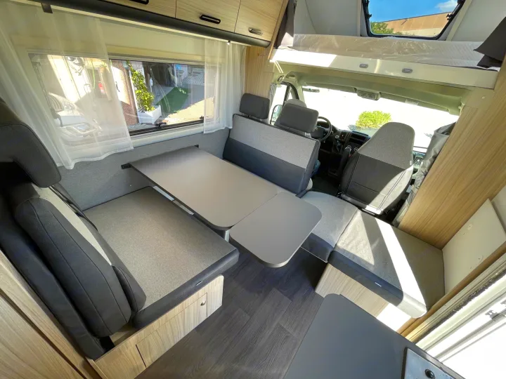 Modern rv rental interior: view of dinette seating, adjustable table, and cab-over sleeping area.. SunLiving A 75 DP 23 2023