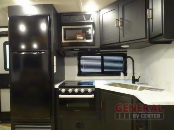 This RV rental features a modern kitchen with black appliances, ample counter space, and storage, perfect for your next trip.. Keystone RV Outback Ultra-Lite 2021