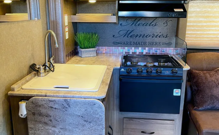 Compact RV rental kitchen with sink, stove, and counter. Features "Meals & Memories" decor, offering home comfort on the road.. Other Other 2016