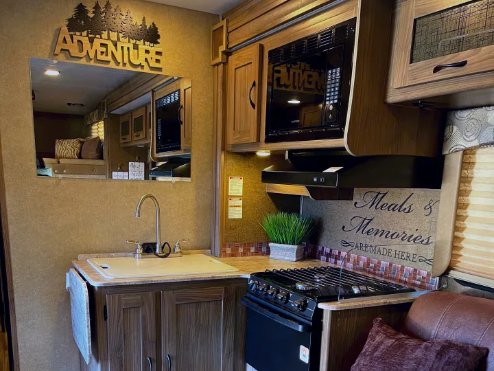 Cozy RV rental kitchen featuring a microwave, stove, sink, and an inspiring "Adventure" wall decor. Perfect for trips!. Other Other 2016