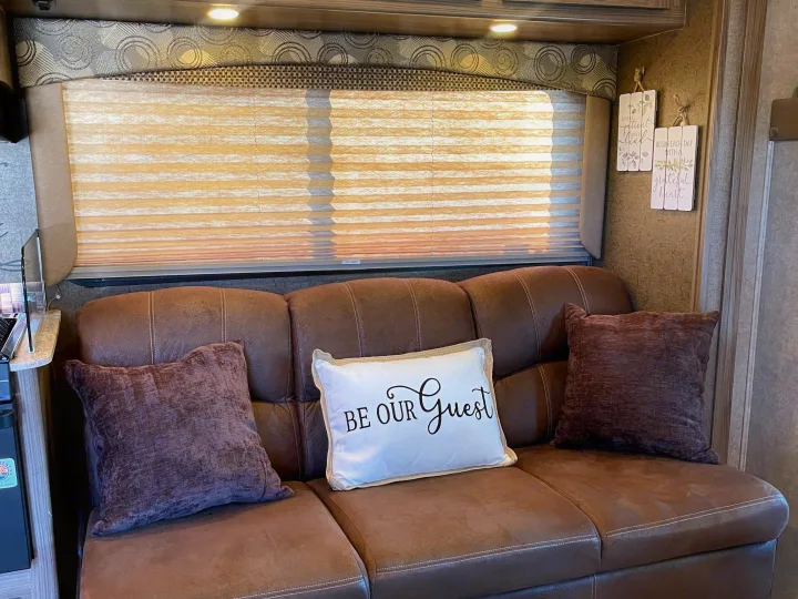 Cozy RV rental interior with a brown sofa, 'Be Our Guest' pillow, and light-filtering window blinds.. Other Other 2016