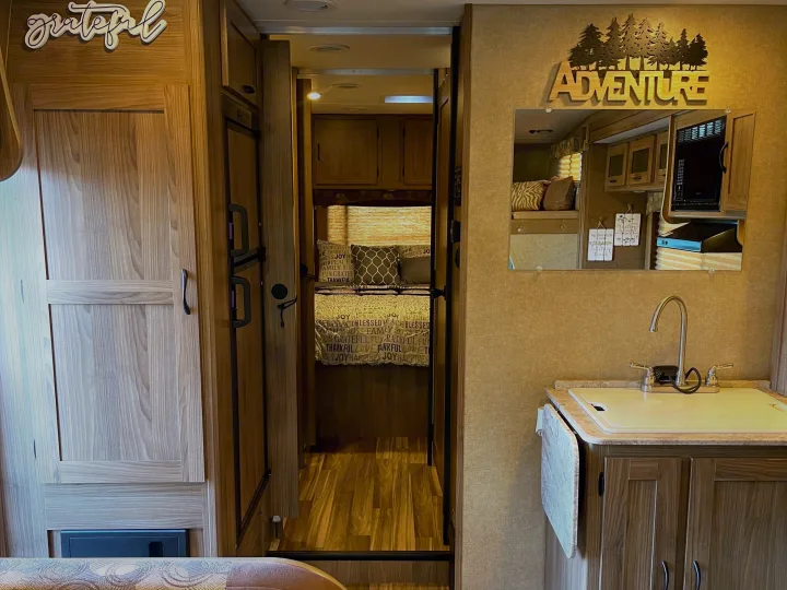 Cozy RV rental interior: kitchen with sink, mirror reflecting microwave & 'Adventure' sign, leads to bedroom.. Other Other 2016