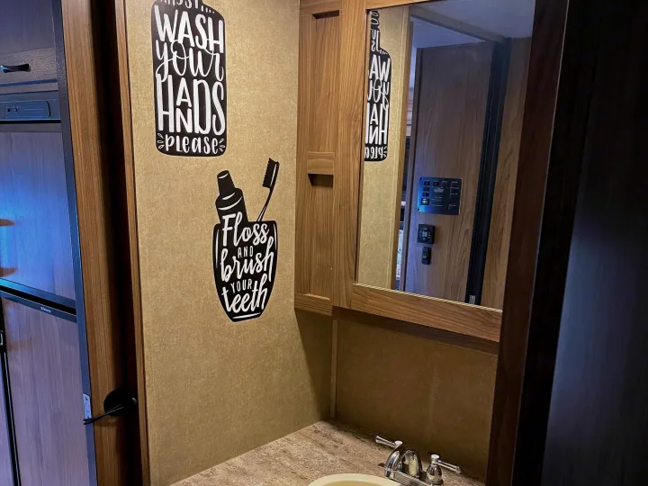 RV rental bathroom featuring a vanity with sink, mirror, and hygiene wall decals. The mirror reflects interior controls.. Other Other 2016