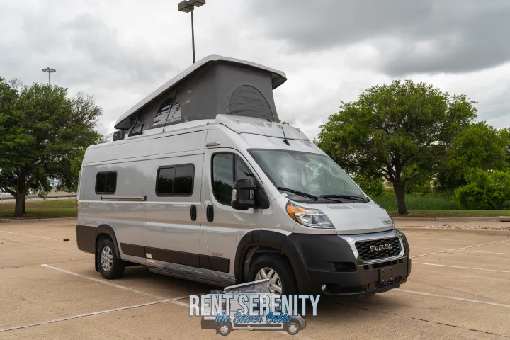 Silver pop-top camper van RV rental, parked in lot. Its roof tent is extended under a cloudy sky.. Winnebago Solis 2023