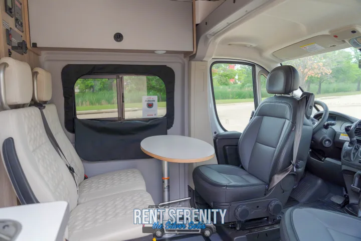 RV rental interior featuring a swiveling front seat, two passenger seats, and a dining table, ready for adventures.. Winnebago Solis 2023
