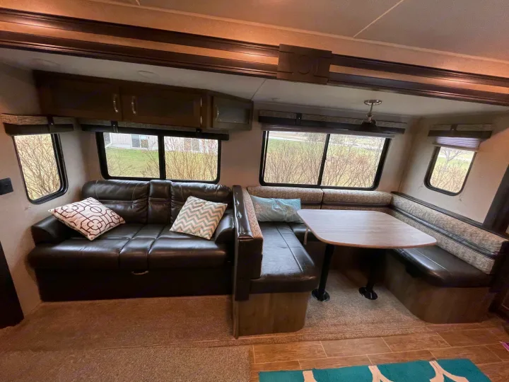 Inside an RV rental: a cozy living and dining area with a black leather sofa, plush pillows, and a booth table.. Forest River Palomino Puma 2019