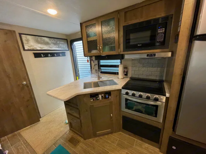 This compact RV kitchen and entry hall features a microwave, stove, sink, and a "Happy Place" sign, perfect for an RV rental.. Forest River Palomino Puma 2019