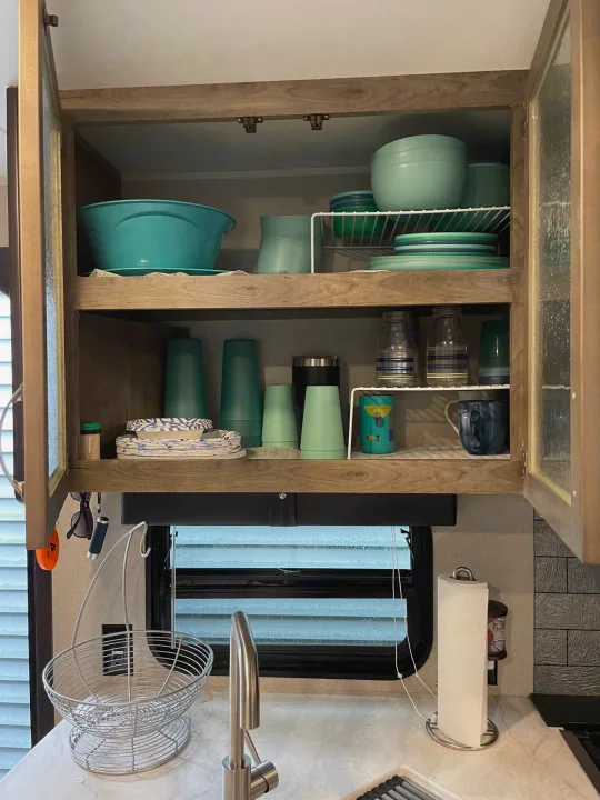 RV rental kitchen cabinet, neatly stocked with teal dishes & cups; counter features sink, basket, paper towels.. Forest River Palomino Puma 2019