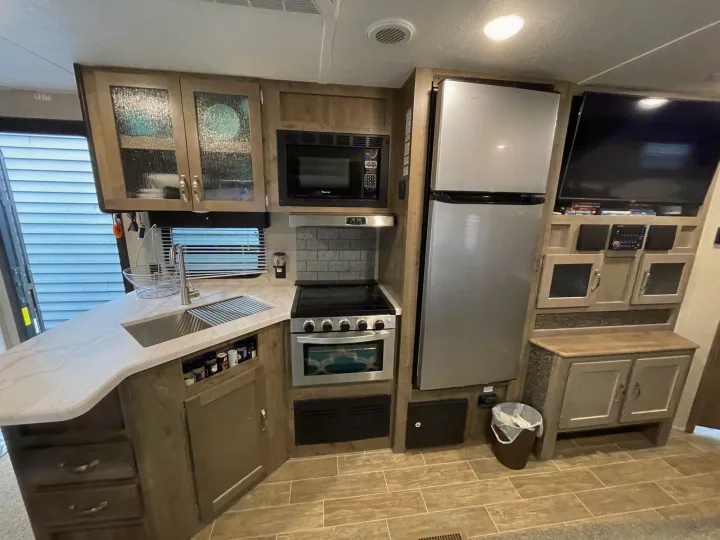 Modern RV rental kitchen with island, stainless appliances, and TV setup for comfortable travel.. Forest River Palomino Puma 2019