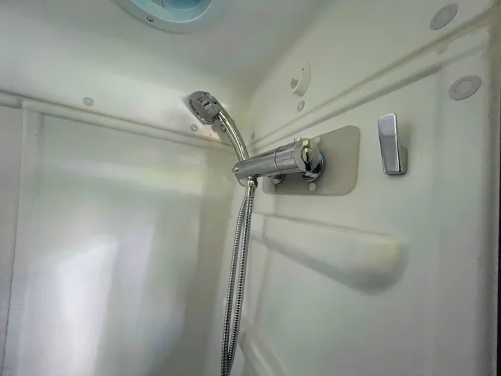 White RV rental shower with chrome handheld showerhead, hose, and faucet. Compact and functional.. Winnebago Mercedes Sprinter 2019