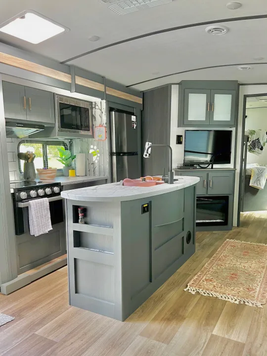 Modern RV rental kitchen featuring a central island, full appliances, and living area with TV.. Keystone Bullet Ultra Lite 2023