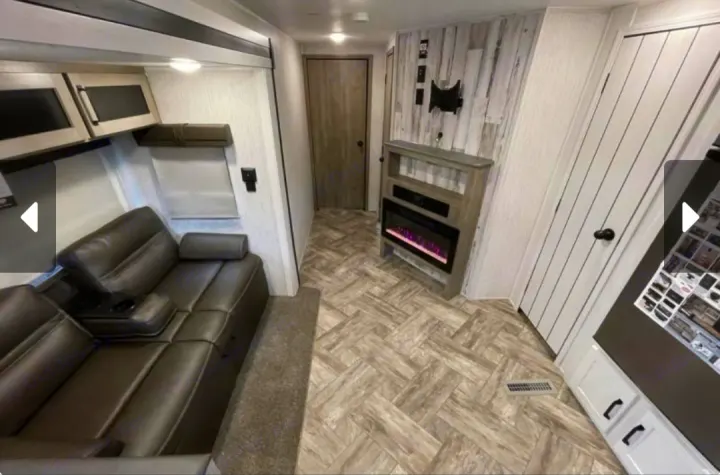 Interior of a modern RV rental featuring a comfortable reclining sofa, electric fireplace, and stylish herringbone flooring.. Forest River Palomino Puma 2023