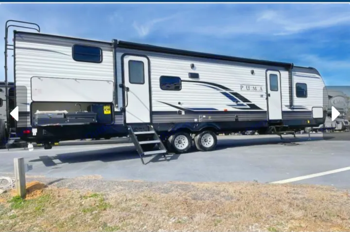 A modern travel trailer, ideal for rv rental, boasts an outdoor kitchen and accessible steps. Sleek white & grey design.. Forest River Palomino Puma 2023