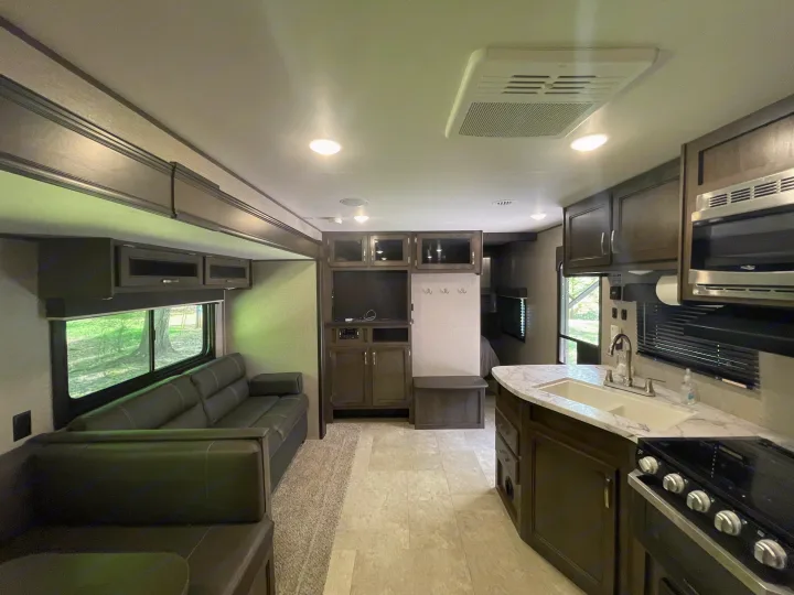 Modern RV rental interior featuring a full kitchen with sink, dark cabinets, a sofa living area, and entertainment center.. Jayco Jay Flight SLX 2021