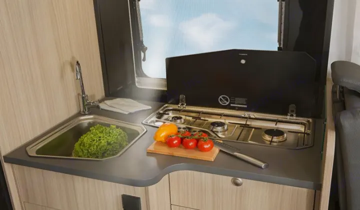 Well-equipped RV rental kitchen: sink with lettuce, two-burner stove, and fresh veggies on a cutting board for cooking.. SunLiving S 72 DL 2023