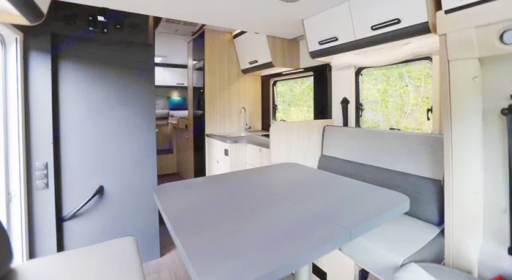 Bright rv rental interior featuring a gray dining table, comfortable bench seats, a compact kitchen, and a bed further back.. SunLiving S 72 DL 2023