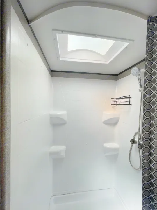 RV rental shower interior: bright, white stall with skylight, built-in shelves, and handheld shower head.. Jayco Jay Flight SLX 2021
