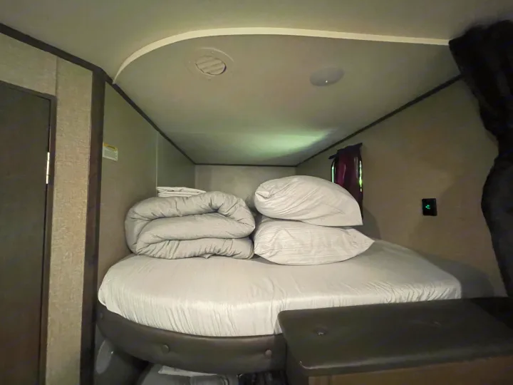 Inside an RV rental: a compact bedroom with neatly arranged bed, pillows, and folded comforter, set for comfortable travel.. Jayco Jay Flight SLX 2021