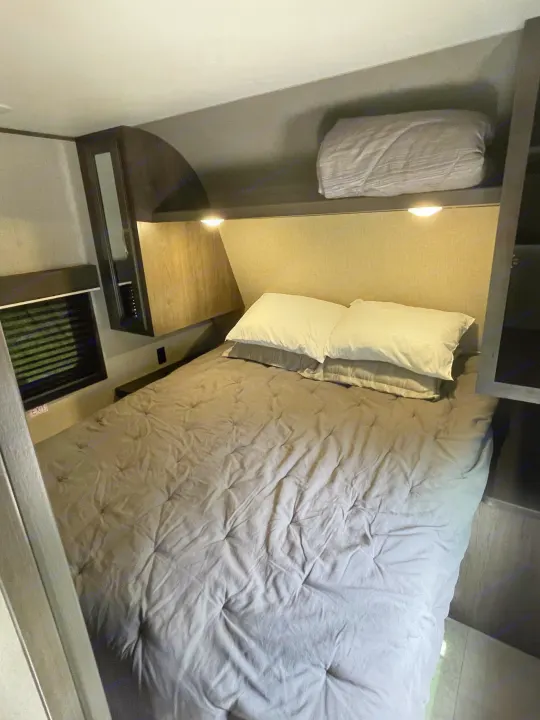 Cozy RV rental bedroom features a gray bed, white pillows, reading lights, and overhead storage.. Jayco Jay Flight SLX 2021