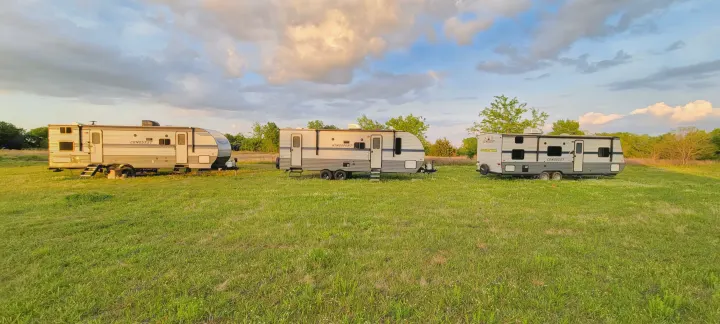 Three distinct RV rental travel trailers (Conquest, Kingsport) in a vibrant green field, ready for your next adventure.. Gulf Stream Conquest 2021