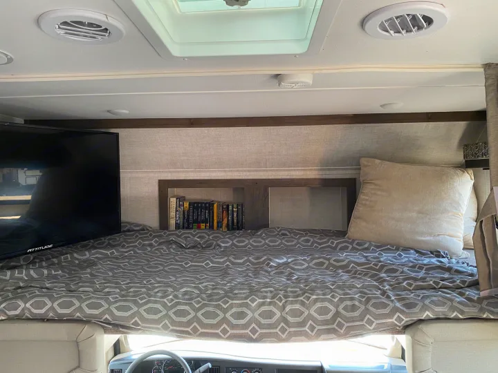 RV rental interior showing a bunk bed with a TV, a built-in bookshelf filled with books, and plush pillows for comfort.. Gulf Stream Conquest 6280LE 2023