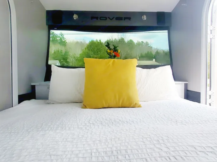 Experience an RV rental! This comfy Rover RV bedroom features a large bed, yellow accent pillow, and panoramic forest views.. Intech Luna Rover 2023