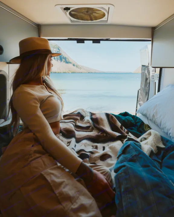 A woman in a hat gazes at a stunning lake view from inside her cozy RV rental, perfect for scenic adventures.. Winnebago Solis 2022