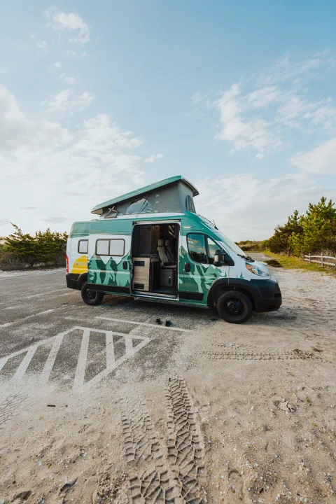 Vibrant green and white RV rental camper van with a pop-top roof and open door, parked on sandy terrain under a blue sky.. Winnebago Solis 2022