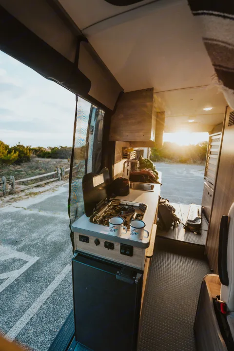 RV rental camper kitchen with stove, sink, and fridge, bathed in golden sunset light. Perfect for mobile adventures.. Winnebago Solis 2022