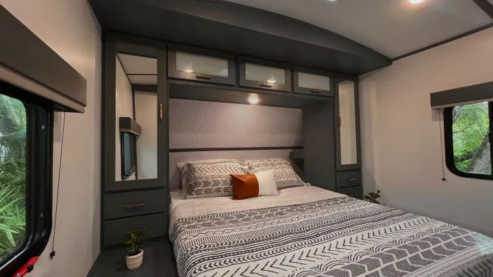 Modern RV rental bedroom featuring a queen bed with patterned bedding, built-in storage, and side windows.. Keystone RV Bullet Ultra Lite 2022