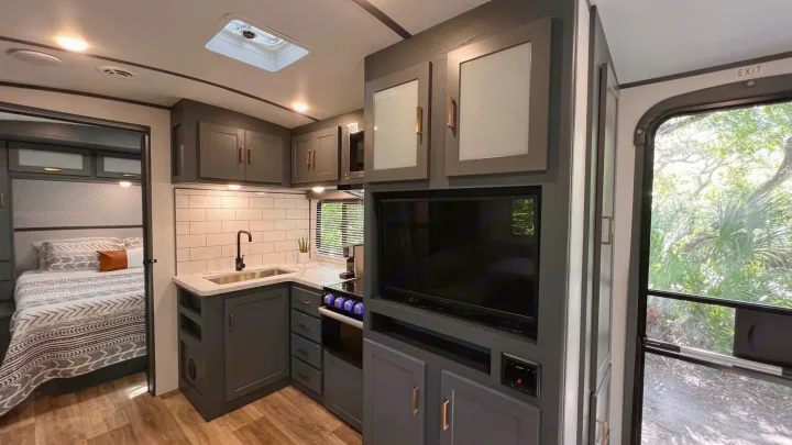 Modern RV rental interior: sleek dark kitchen, TV, and bedroom; a nature view outside the exit door.. Keystone RV Bullet Ultra Lite 2022