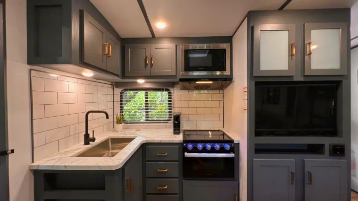 Spacious RV rental kitchen with gray cabinets, marble-look counters, subway tile backsplash, modern appliances, and TV.. Keystone RV Bullet Ultra Lite 2022