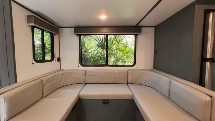 RV rental interior with a comfortable U-shaped dinette, light cushions, and large windows revealing lush greenery.. Keystone RV Bullet Ultra Lite 2022