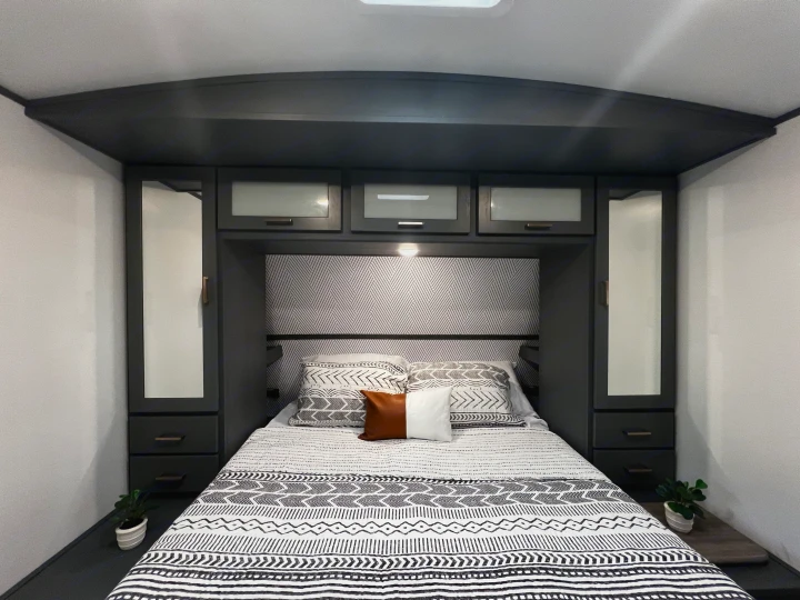 Modern RV rental bedroom with black and white patterned bedding, dark storage cabinets, and ambient lighting. Features bedside plants.. Keystone RV Bullet Ultra Lite 2022