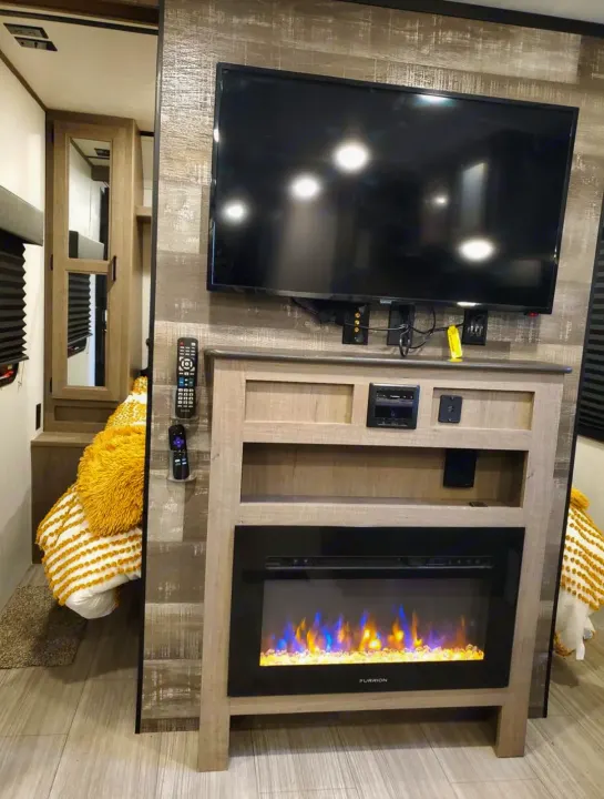 This RV rental's cozy interior features a wall-mounted TV, electric fireplace with blue & orange flames, and a comfortable bed.. Keystone RV Hideout Luxury 2021