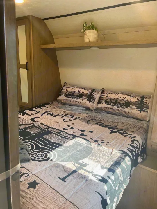 Cozy RV rental bedroom featuring a "Happy Camping" themed bed, built-in storage, and an overhead shelf.. Keystone RV Hideout Luxury 2021
