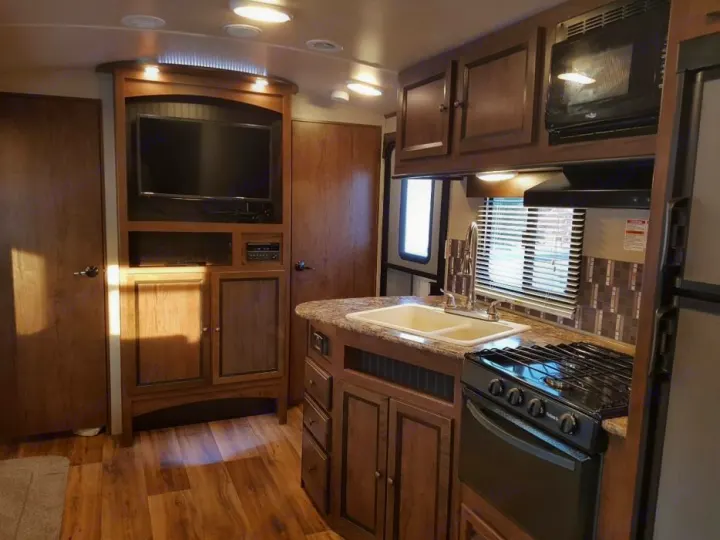 This modern RV rental interior features a kitchen with a sink & stove, TV area, & wood cabinetry.. Cruiser RV MPG Ultra Lite 2017