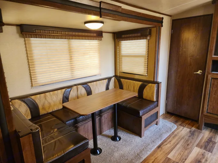 Spacious RV rental dining booth with dark brown seating, a light wood table, and pleated window blinds for comfortable meals.. Cruiser RV MPG Ultra Lite 2017