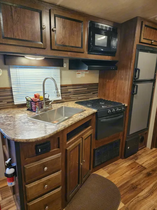 RV rental kitchen: Wood cabinets, sink, stovetop, microwave, and fridge visible, ideal for your next trip.. Cruiser RV MPG Ultra Lite 2017