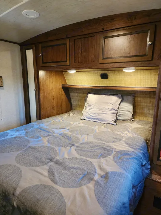 Interior of an RV rental bedroom showing a bed, wood storage cabinets, and LED overhead lights.. Cruiser RV MPG Ultra Lite 2017