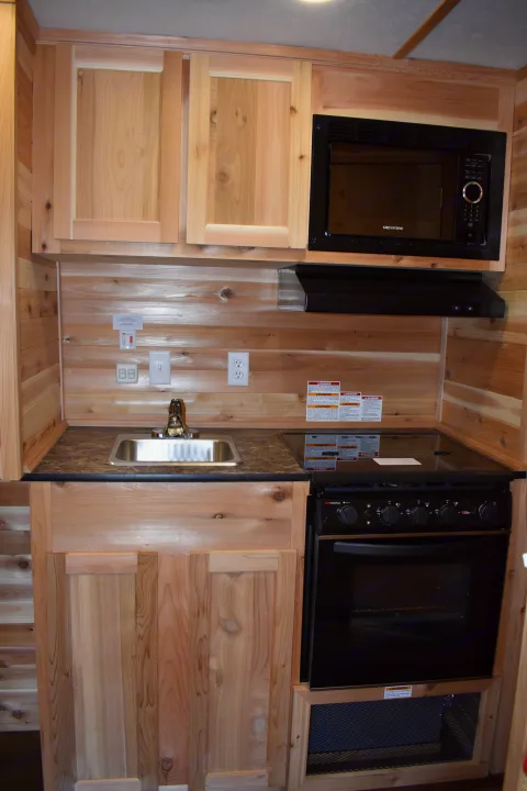 Inside an RV rental: a cozy kitchen area with natural wood cabinets, microwave, sink, and oven for your travel cooking needs.. Ice Castle Fish Houses Rv Edition Standard 2024