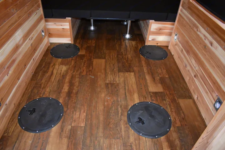 RV rental interior: cozy wood-paneled space with a dark wood floor, four ice fishing floor covers, and a seating area.. Ice Castle Fish Houses Rv Edition Standard 2024